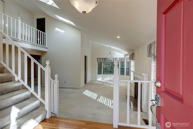 entrance foyer featuring a skylight, stairway, high vaulted ceiling, and light wood finished floors