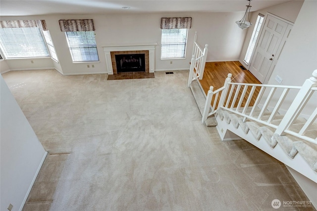 unfurnished living room with stairs, baseboards, a fireplace, and carpet flooring