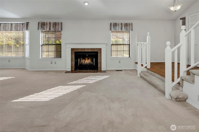 unfurnished living room with a tile fireplace, baseboards, vaulted ceiling, stairway, and carpet