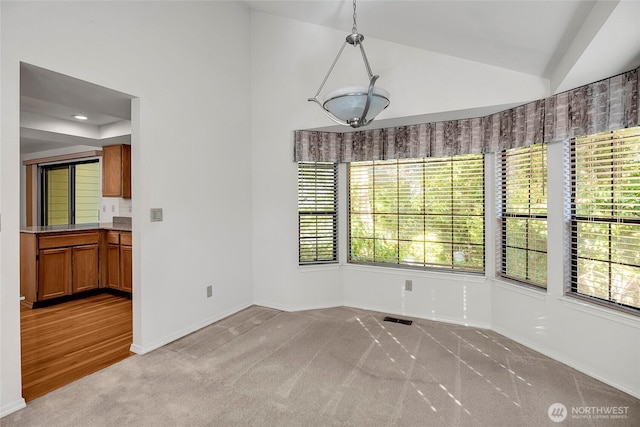 unfurnished dining area featuring lofted ceiling, baseboards, visible vents, and light colored carpet