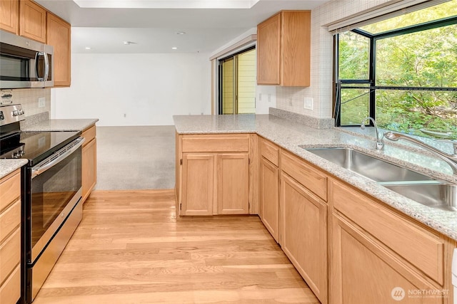 kitchen featuring light wood finished floors, light brown cabinetry, appliances with stainless steel finishes, and a sink