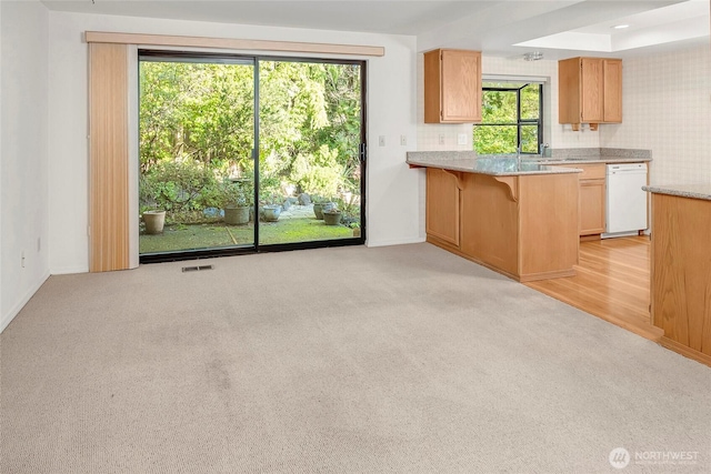 kitchen featuring light carpet, dishwasher, visible vents, and a kitchen bar