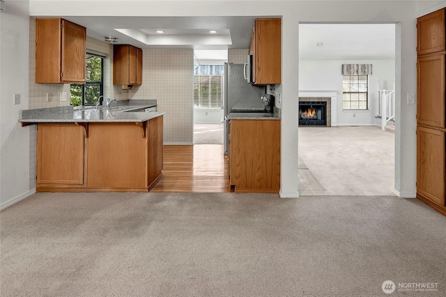 kitchen with light carpet, brown cabinetry, a tray ceiling, and open floor plan