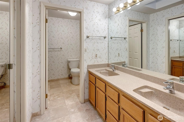 bathroom featuring toilet, wallpapered walls, and a sink