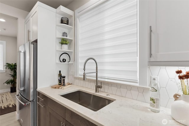 kitchen with light stone counters, a sink, backsplash, freestanding refrigerator, and open shelves