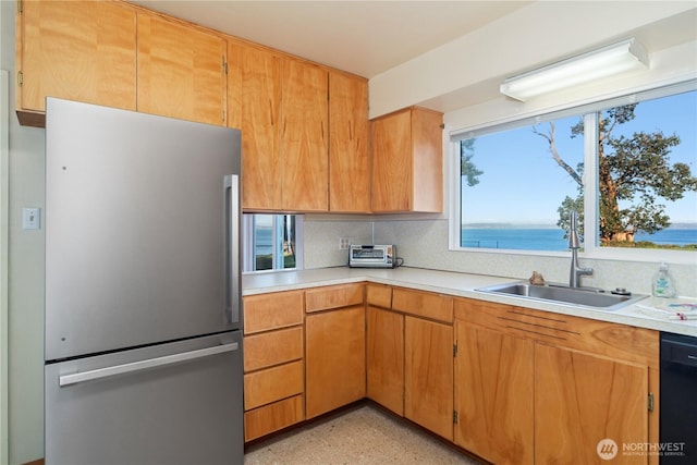 kitchen with dishwasher, freestanding refrigerator, a sink, light countertops, and backsplash