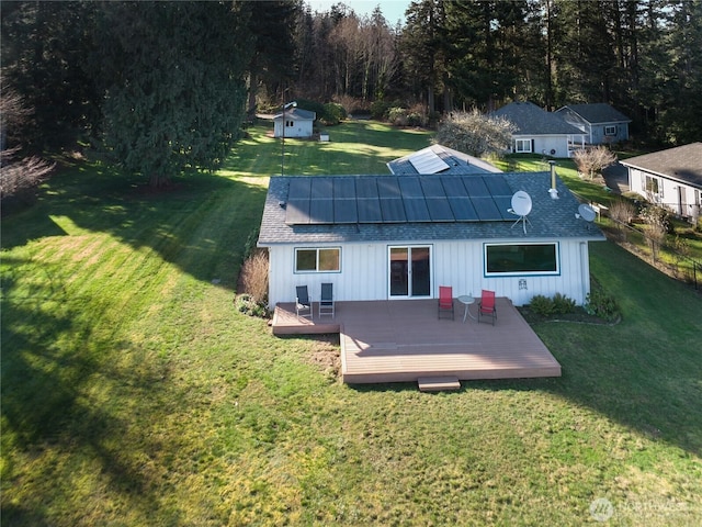 back of house featuring a yard, roof with shingles, solar panels, and a wooden deck