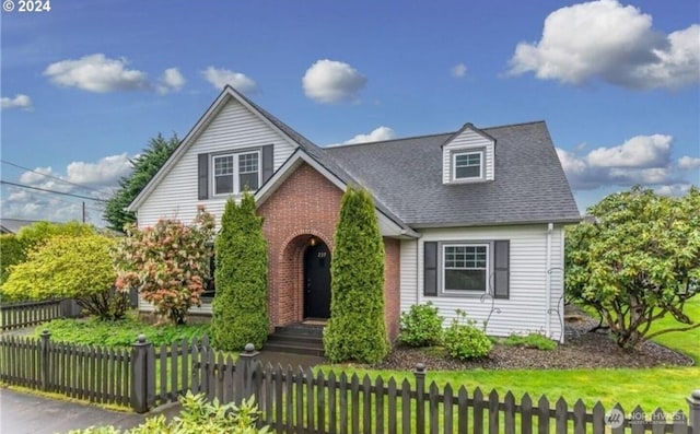 view of front of house with a fenced front yard, a front yard, brick siding, and roof with shingles