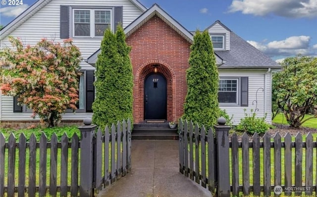 view of front of home with brick siding, a fenced front yard, and a shingled roof