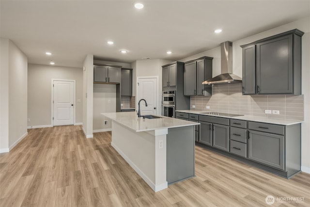 kitchen with wall chimney range hood, backsplash, light wood-style floors, and black electric cooktop