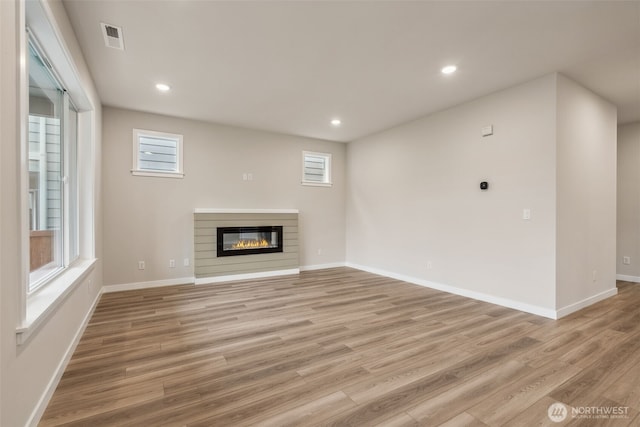 unfurnished living room featuring a glass covered fireplace, light wood-type flooring, baseboards, visible vents, and recessed lighting