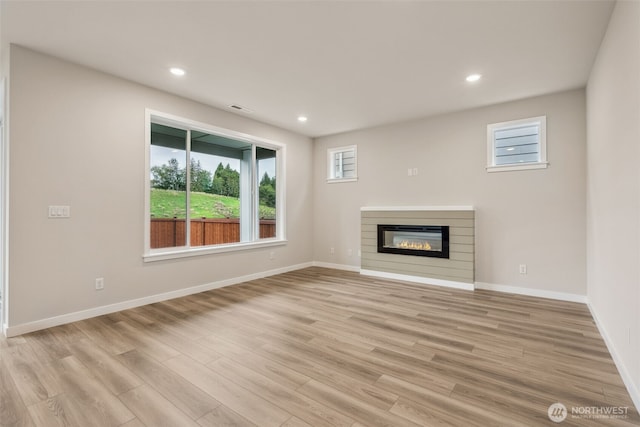 unfurnished living room with visible vents, a glass covered fireplace, baseboards, recessed lighting, and light wood-style floors