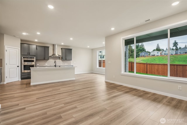 unfurnished living room featuring light wood finished floors, a sink, baseboards, visible vents, and recessed lighting