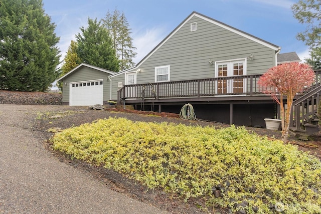 view of front of property with a deck, aphalt driveway, a detached garage, and an outbuilding