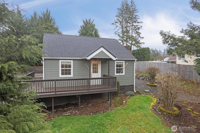 view of front of house featuring a front lawn, roof with shingles, fence, and a wooden deck