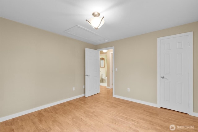 unfurnished bedroom featuring light wood-style flooring, baseboards, and attic access