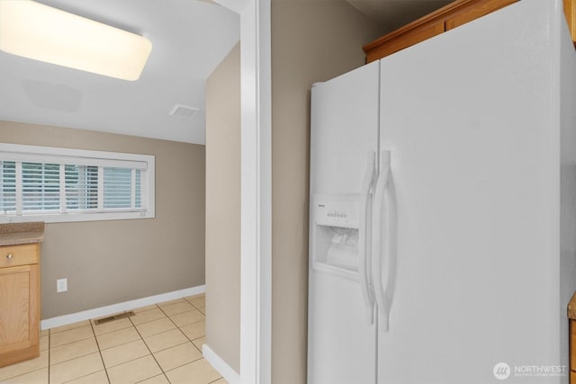 kitchen featuring white fridge with ice dispenser, light tile patterned flooring, visible vents, and baseboards