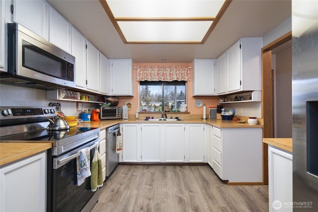 kitchen with light wood finished floors, light countertops, appliances with stainless steel finishes, white cabinetry, and a sink