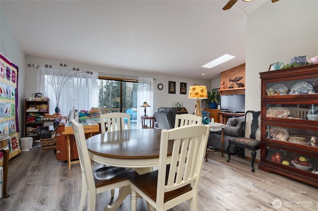 dining area with light wood-style floors, vaulted ceiling with skylight, and ceiling fan