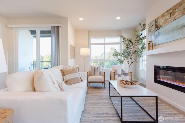 living room featuring a healthy amount of sunlight, recessed lighting, baseboards, and a glass covered fireplace