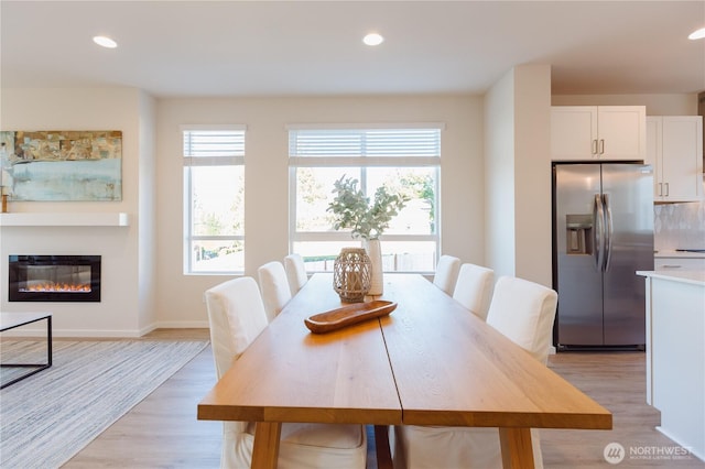 dining area featuring plenty of natural light, a glass covered fireplace, light wood-style flooring, and recessed lighting