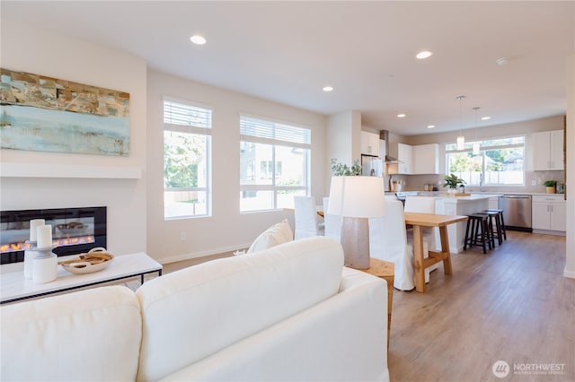 living area featuring light wood finished floors, baseboards, a glass covered fireplace, and recessed lighting