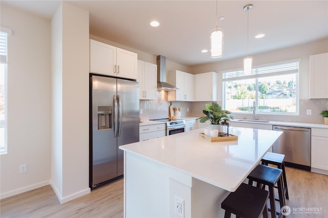 kitchen with decorative backsplash, appliances with stainless steel finishes, a sink, wall chimney range hood, and a kitchen bar