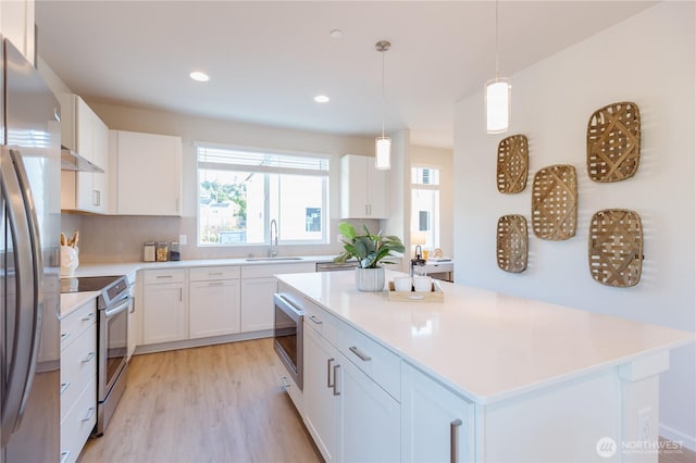 kitchen featuring a sink, light wood-style floors, light countertops, appliances with stainless steel finishes, and a center island