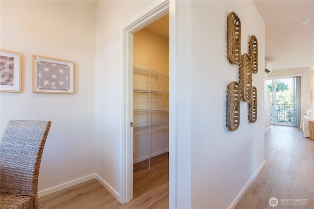 hall with light wood-type flooring, a wall unit AC, and baseboards