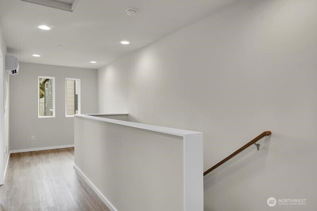 hallway with an AC wall unit, wood finished floors, an upstairs landing, and baseboards