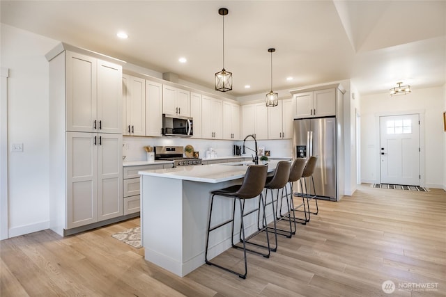 kitchen featuring a kitchen island with sink, a sink, a breakfast bar area, light countertops, and appliances with stainless steel finishes
