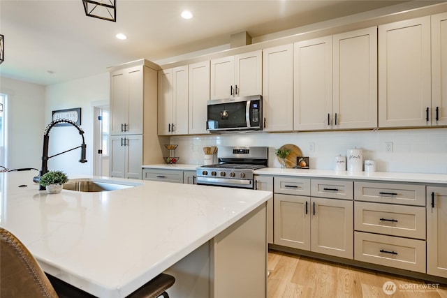 kitchen with recessed lighting, light wood finished floors, a sink, decorative backsplash, and appliances with stainless steel finishes