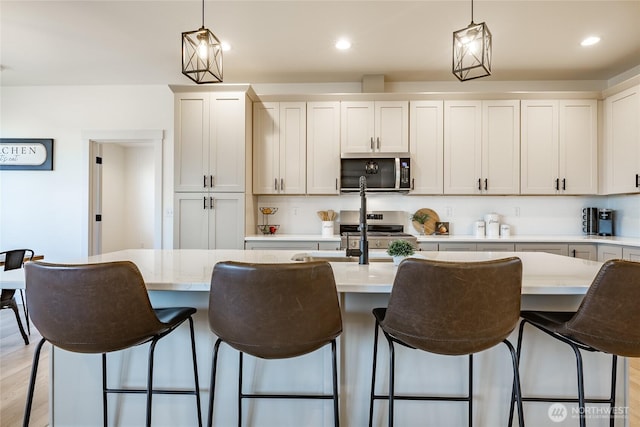 kitchen with a breakfast bar area, stainless steel appliances, a center island with sink, and hanging light fixtures
