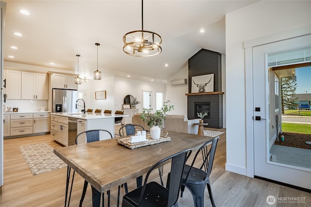 dining room with a brick fireplace, an AC wall unit, light wood-style flooring, and lofted ceiling