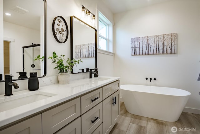 bathroom featuring double vanity, visible vents, a freestanding tub, and a sink