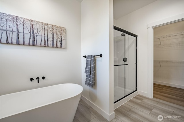 full bathroom with wood finished floors, a shower stall, a freestanding tub, baseboards, and a spacious closet