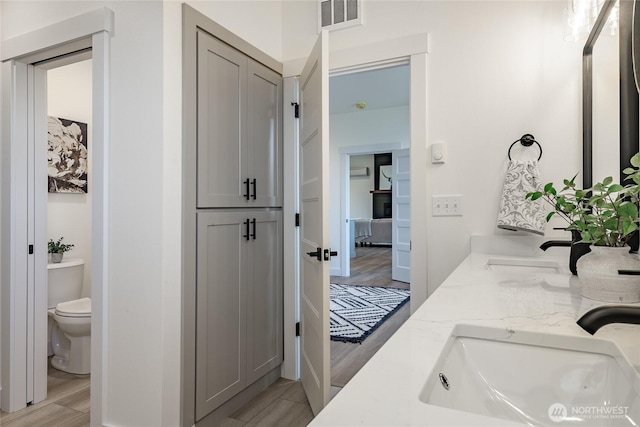 bathroom with toilet, double vanity, a sink, and visible vents