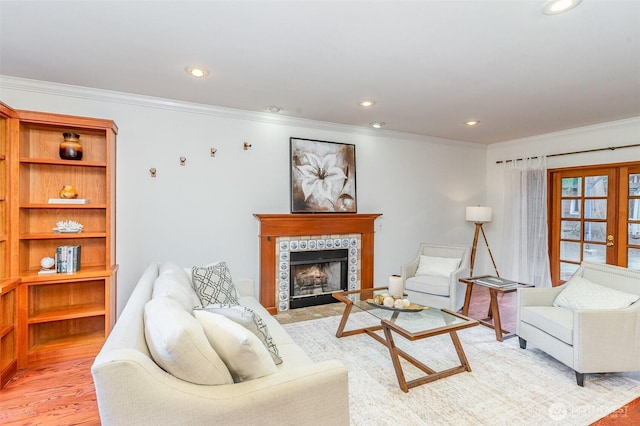 living room with light wood-type flooring, a tile fireplace, crown molding, and french doors