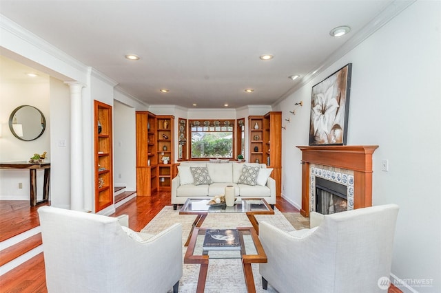 living room featuring a fireplace, decorative columns, recessed lighting, ornamental molding, and wood finished floors