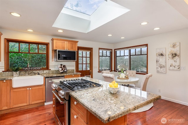 kitchen with a kitchen island, light stone countertops, stainless steel appliances, light wood-type flooring, and a sink