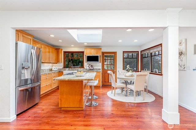 kitchen with a skylight, a center island, light wood-type flooring, stainless steel fridge, and a kitchen bar