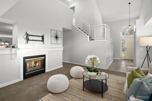 carpeted living area featuring stairs, high vaulted ceiling, a glass covered fireplace, and baseboards