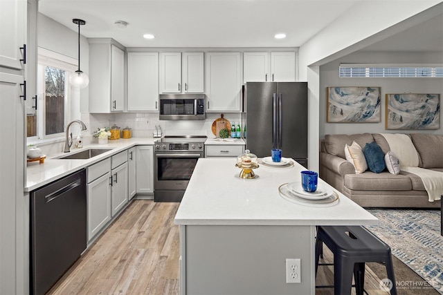 kitchen with a sink, a kitchen breakfast bar, open floor plan, light countertops, and appliances with stainless steel finishes