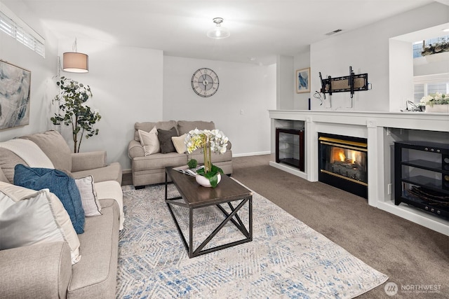 carpeted living area featuring a glass covered fireplace, visible vents, and baseboards