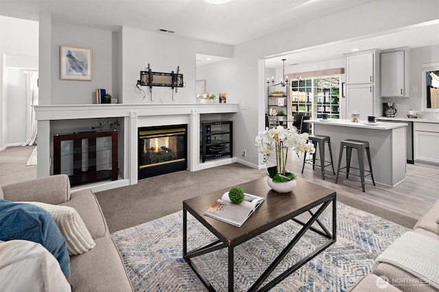 living area featuring visible vents, light colored carpet, a glass covered fireplace, a chandelier, and baseboards