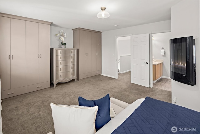 carpeted bedroom with ensuite bath, baseboards, and two closets