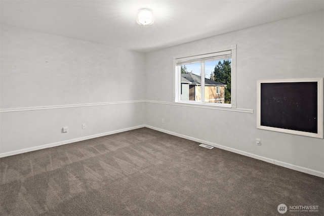 spare room featuring dark carpet, visible vents, and baseboards