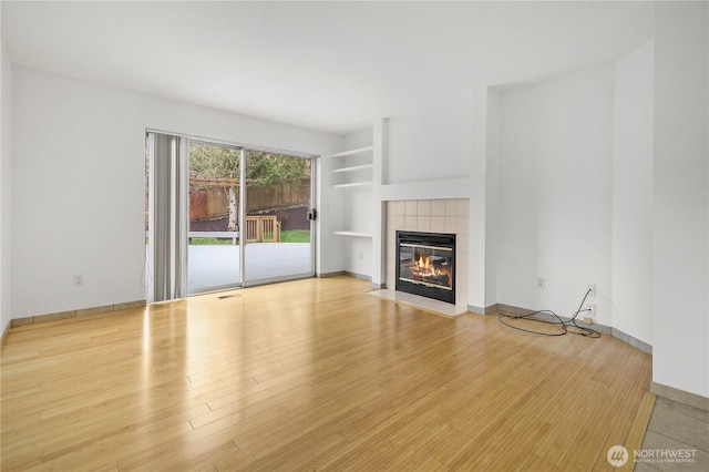 unfurnished living room featuring visible vents, a tile fireplace, baseboards, and wood finished floors