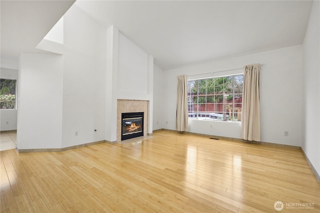 unfurnished living room featuring baseboards, visible vents, light wood finished floors, high vaulted ceiling, and a tiled fireplace