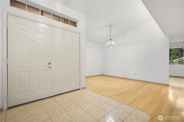 entryway with lofted ceiling, a notable chandelier, light tile patterned floors, and baseboards